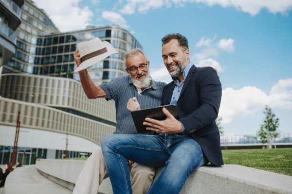 Father and adult son sharing a joyful moment, watching something in tablet. Fathers day concept.
