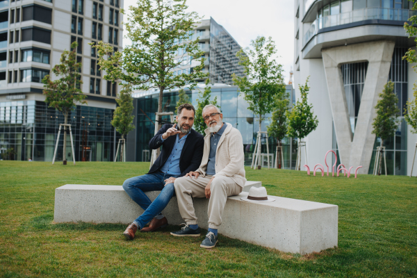 Father and adult son sitting on bench in park, sharing peaceful moment. Fathers day concept.