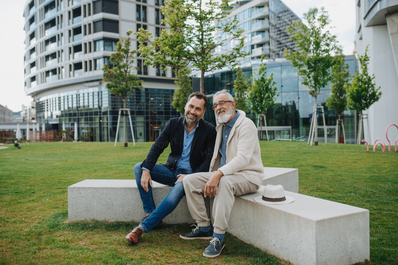 Father and adult son sitting on bench in park, sharing peaceful moment. Fathers day concept.