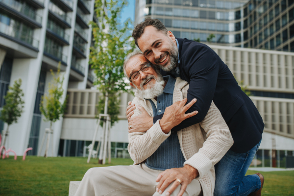 Father and adult son sitting on bench in park, sharing peaceful moment. Fathers day concept.