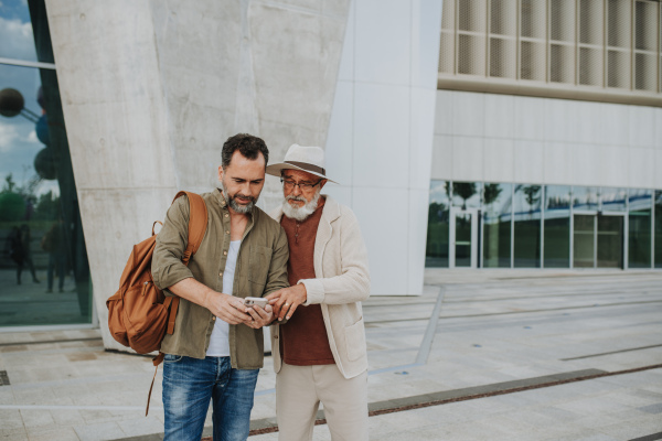 Mature son and father traveling together, looking at map on smartphone.