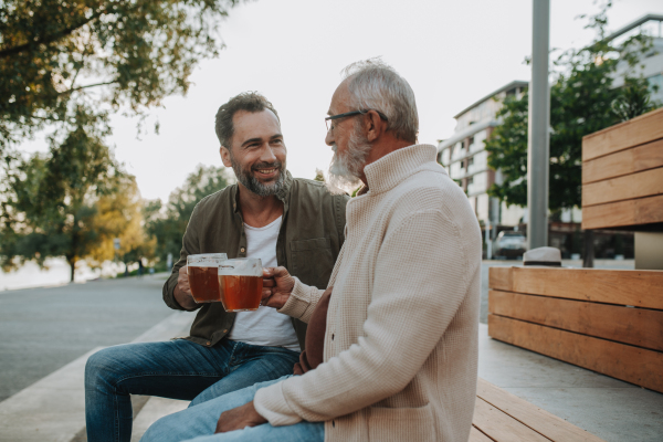 Smiling dad and adult son enjoying cold beer outdoors. Fathers day concept.