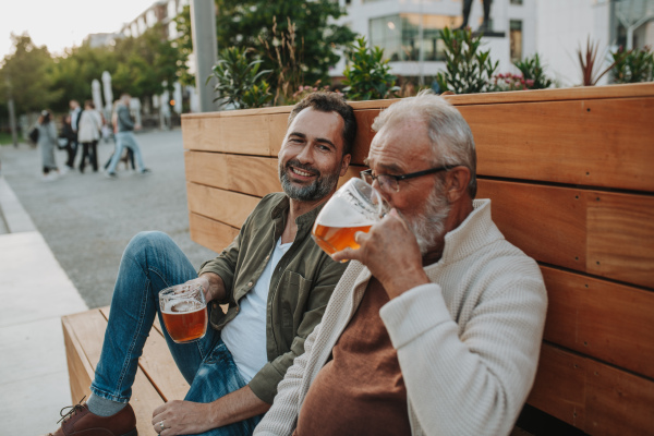 Smiling dad and adult son enjoying cold beer outdoors. Fathers day concept.