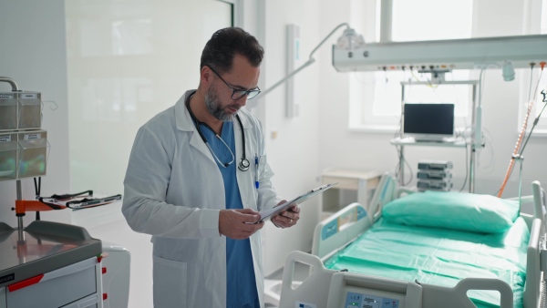 A doctor in a white coat checking a hospital room and filling out a medical form on a clipboard