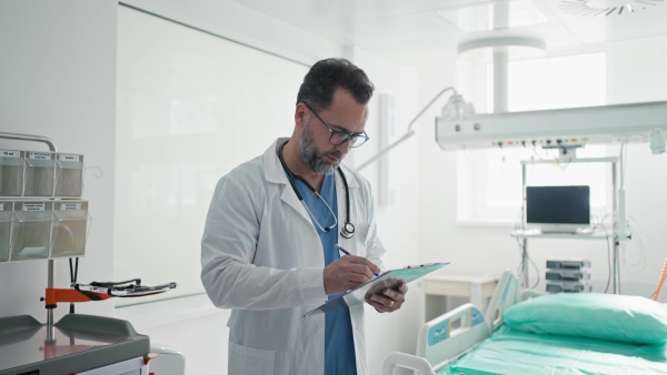 A doctor in a white coat checking a hospital room and filling out a medical form on a clipboard