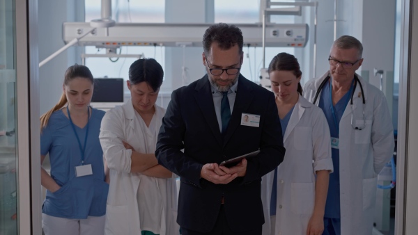 A manager with doctors standing in hospital room and looking at camera.