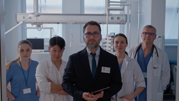 A manager with doctors standing in hospital room and looking at camera.