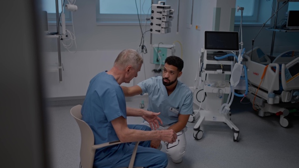 Male nurse comforting a doctor after unsuccessful surgery in hospital corridor.