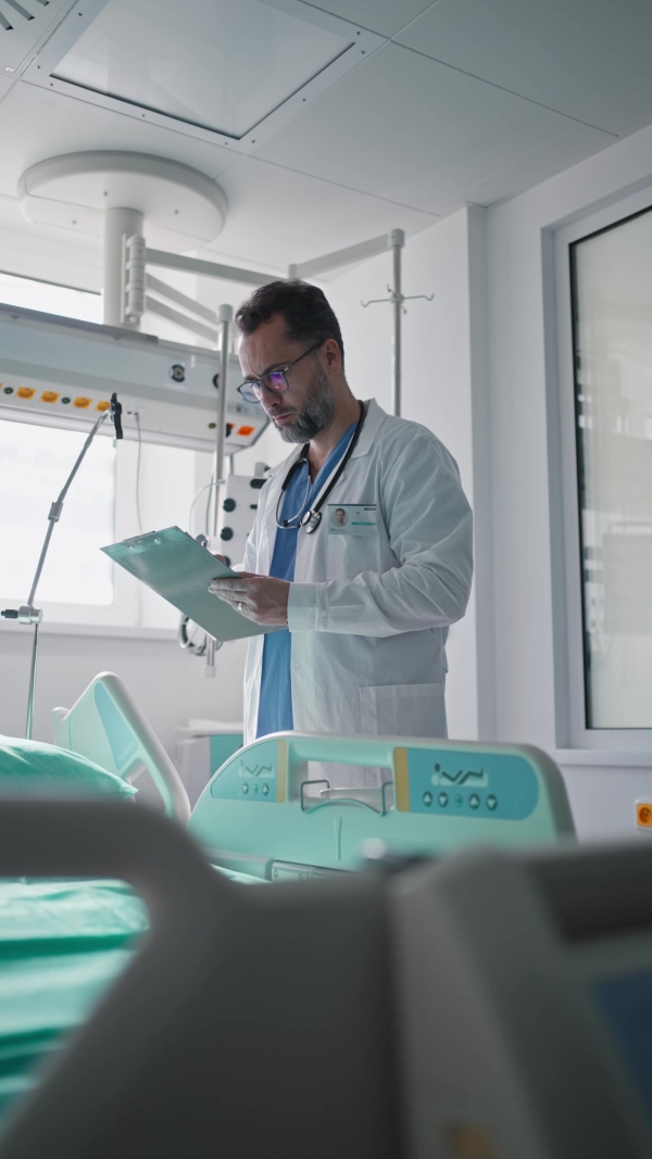 A doctor in a white coat checking a hospital room and filling out a medical form on a clipboard