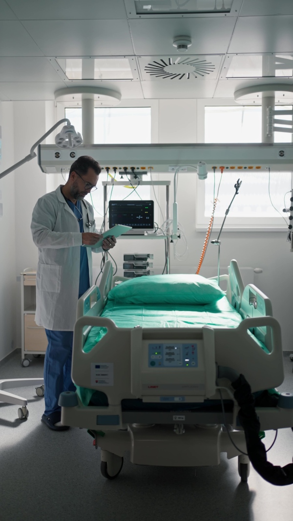 A doctor in a white coat checking a hospital room and filling out a medical form on a clipboard