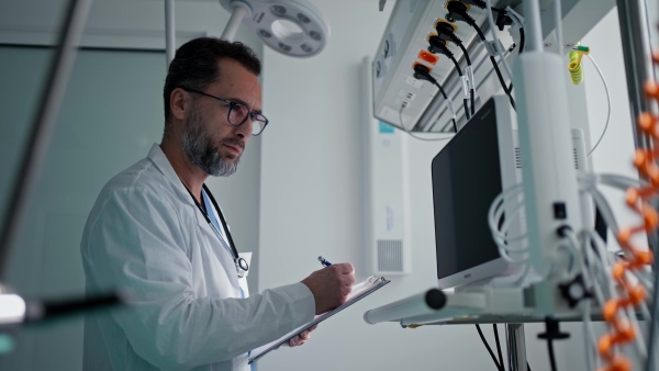 A doctor in a white coat checking a hospital room and filling out a medical form on a clipboard