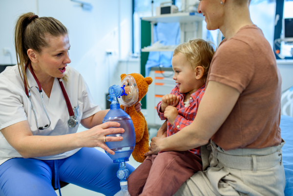 Female pediatrician demonstrates oxygen mask on teddy bear to young patient