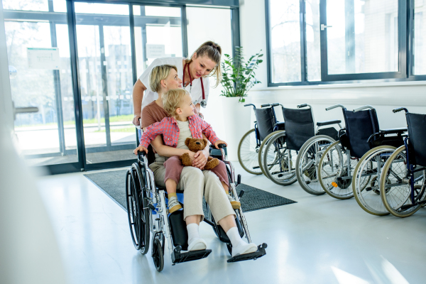 Female doctor or nurse pushing wheelchair with mother and son after treatment