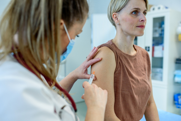 Doctor administering vaccine to woman's arm during routine immunization. Disease prevention.