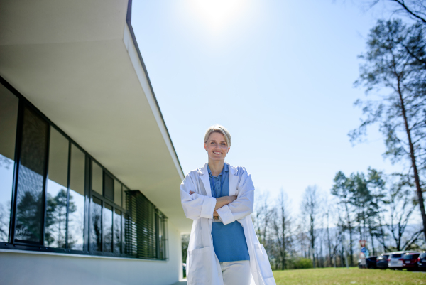 Young female doctor taking a break, standing in front of hospital building.