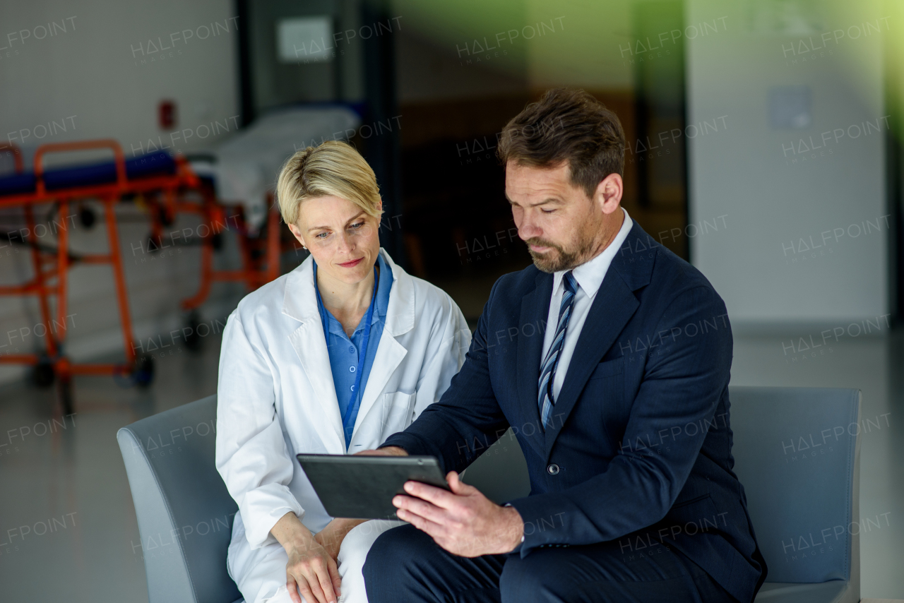 Pharmaceutical sales representative introducing new medication to female doctor, showing her presentation on tablet.