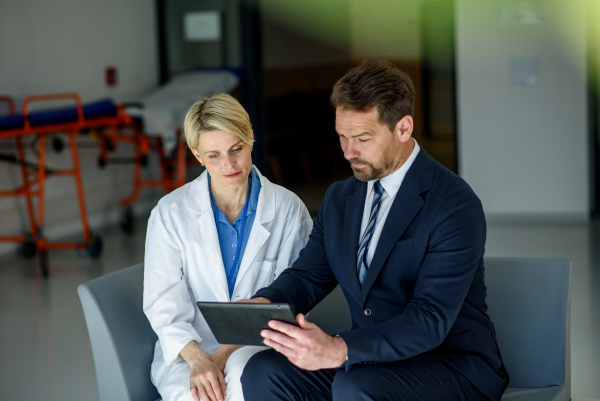 Pharmaceutical sales representative introducing new medication to female doctor, showing her presentation on tablet.