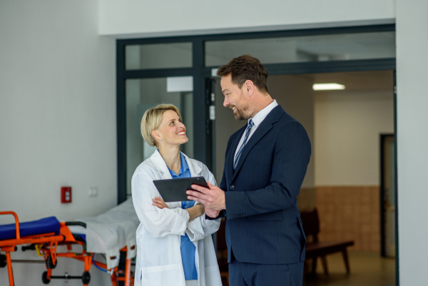 Pharmaceutical sales representative introducing new medication to female doctor, showing her presentation on tablet.
