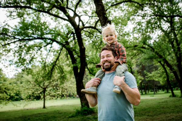 Dad carrying his smiling son on shoulders during walk in park