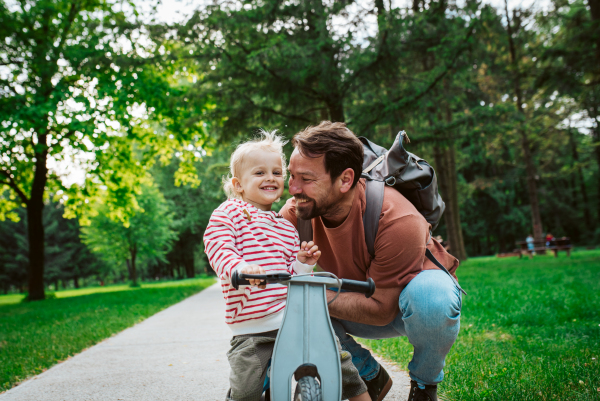 Toddler riding balance bike with dad cheering behind and running behind him.