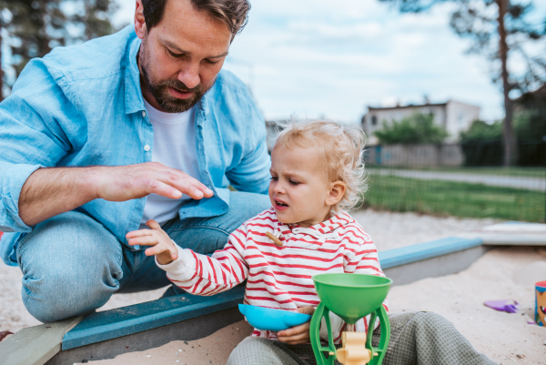 Father and little toddler son playing in the sandbox on playground, weekend fun.