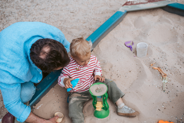 Top view of dad and son playing in the sandbox on playground., weekend fun.
