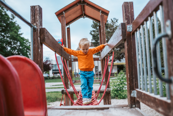 Toddler crossing playground obstacle bridge, weekend activity.