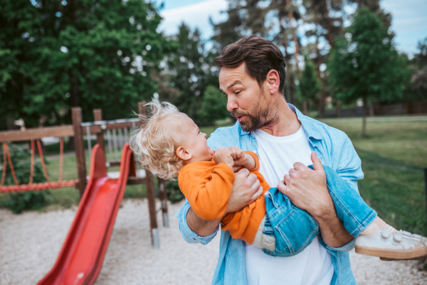 Father playing with toddler son outdoors in city park