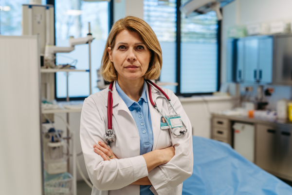 Portrait of female doctor standing in examination room. Medical setting.