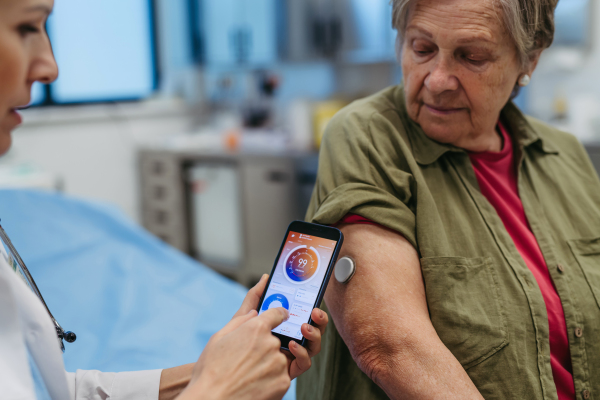 Endocrinologist teaching older patient how to connect continuous glucose monitor with mobil app. Senior health care.