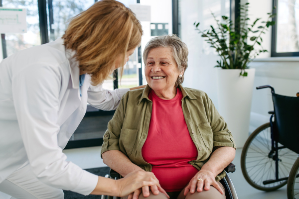 Geriatric doctor talking with patient in a wheelchair in hospital hallway. Senior health care.