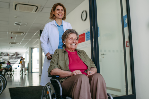 Geriatric doctor pushing a patient in a wheelchair down a hospital hallway. Senior health care.