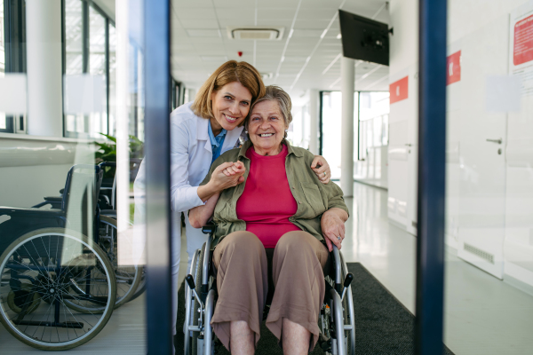 Elderly patient in wheelchair and female physician smiling at clinic. Senior health care.