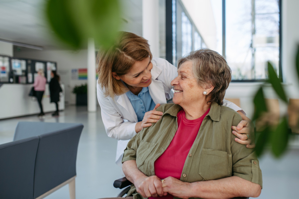 Geriatric doctor talking with patient in a wheelchair in hospital hallway. Senior health care.