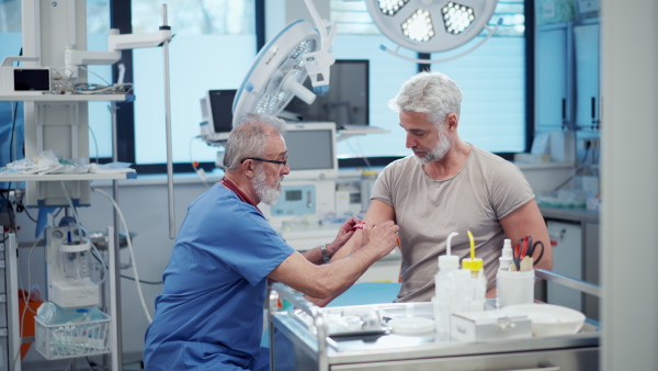 Older doctor drawing blood from patient's arm during medical examination.