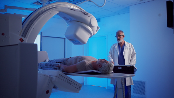 Radiologist performing X-ray examination on male patient using a tilting radiographic wall stand.