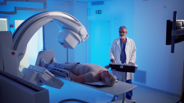Radiologist performing X-ray examination on male patient using a tilting radiographic wall stand.
