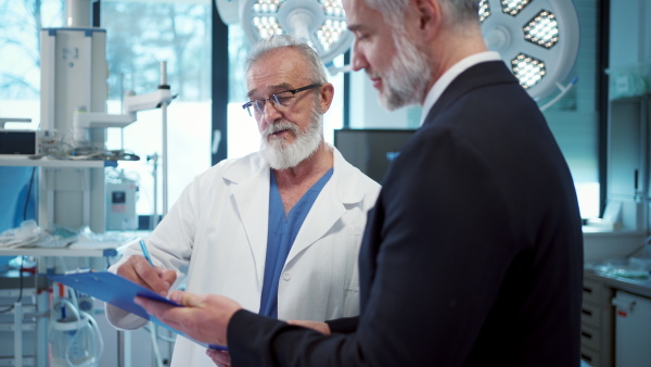 Medical sales representative presenting new medication to doctors, standing in examination room. Hospital setting.