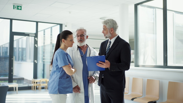 Medical sales representative presenting new medication to doctors, standing hospital hallway. Hospital setting.