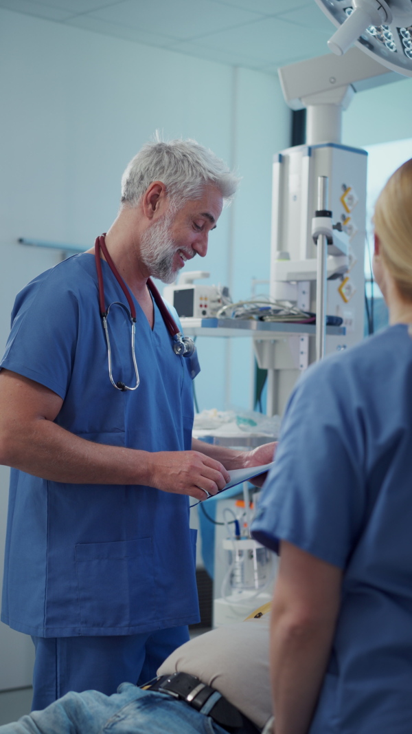 Medical professional examining health record patient lying on examination table while nurse describing the issues. Emergency room setting.