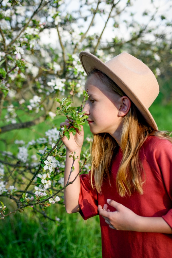 Young girl surrounded by trees smelling delicate blooming flower on branch.