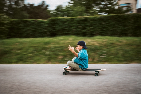 Young boy riding longborad while sitting on it, having fun.