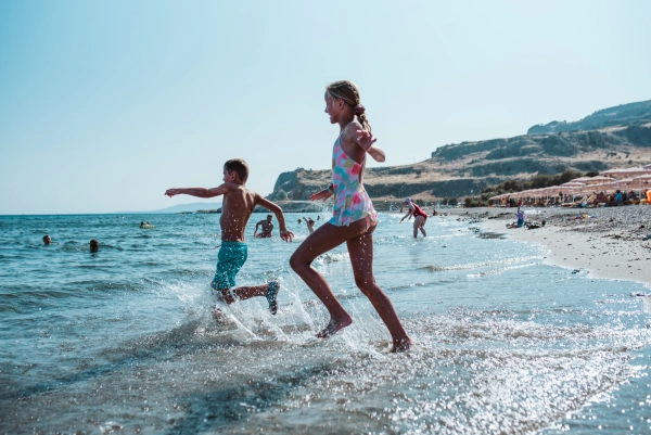 Girl and boy running into water during summer beach holiday.