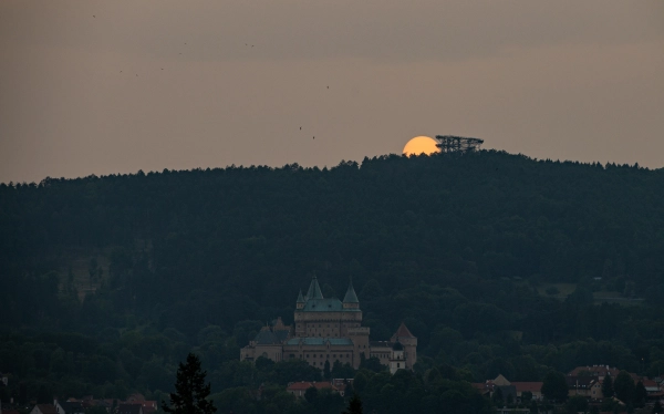 Bojnice Castle at sunset under the forested hills.