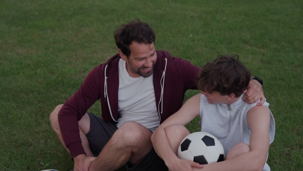Video of dad and teen boy sitting on grass after soccer game. Fathers day concept.